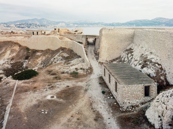 Foto von einem Graben mit einem Haus aus Stein, dahinter eine Mauer aus Stein, dahinter der Blick auf das Meer