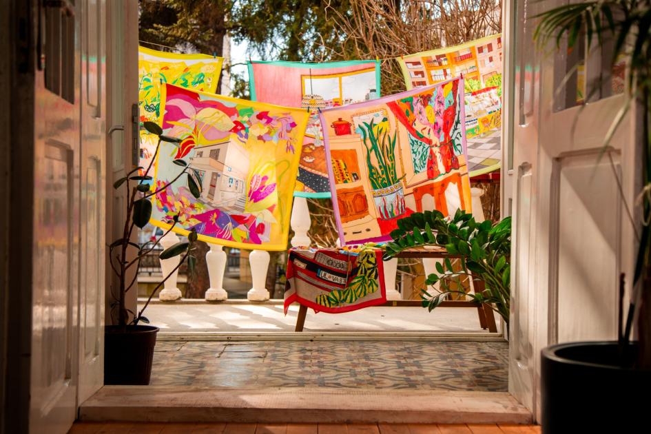 Blick auf einen Balkon hinaus, dort sind illustrierte Stoffquadrate auf Leinen aufgehangen