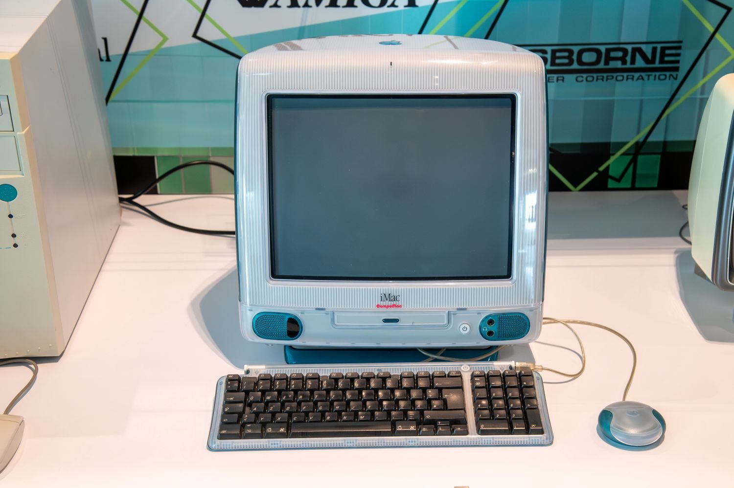 Foto: Apple iMac G3 in Blau mit Tastatur und runder Maus, Ausstellungsansicht auf Tisch.