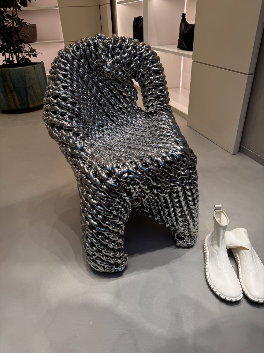 Skulpturaler Stuhl aus grauen, geknoteten Kabeln im Showroom; daneben weiße Stiefel.