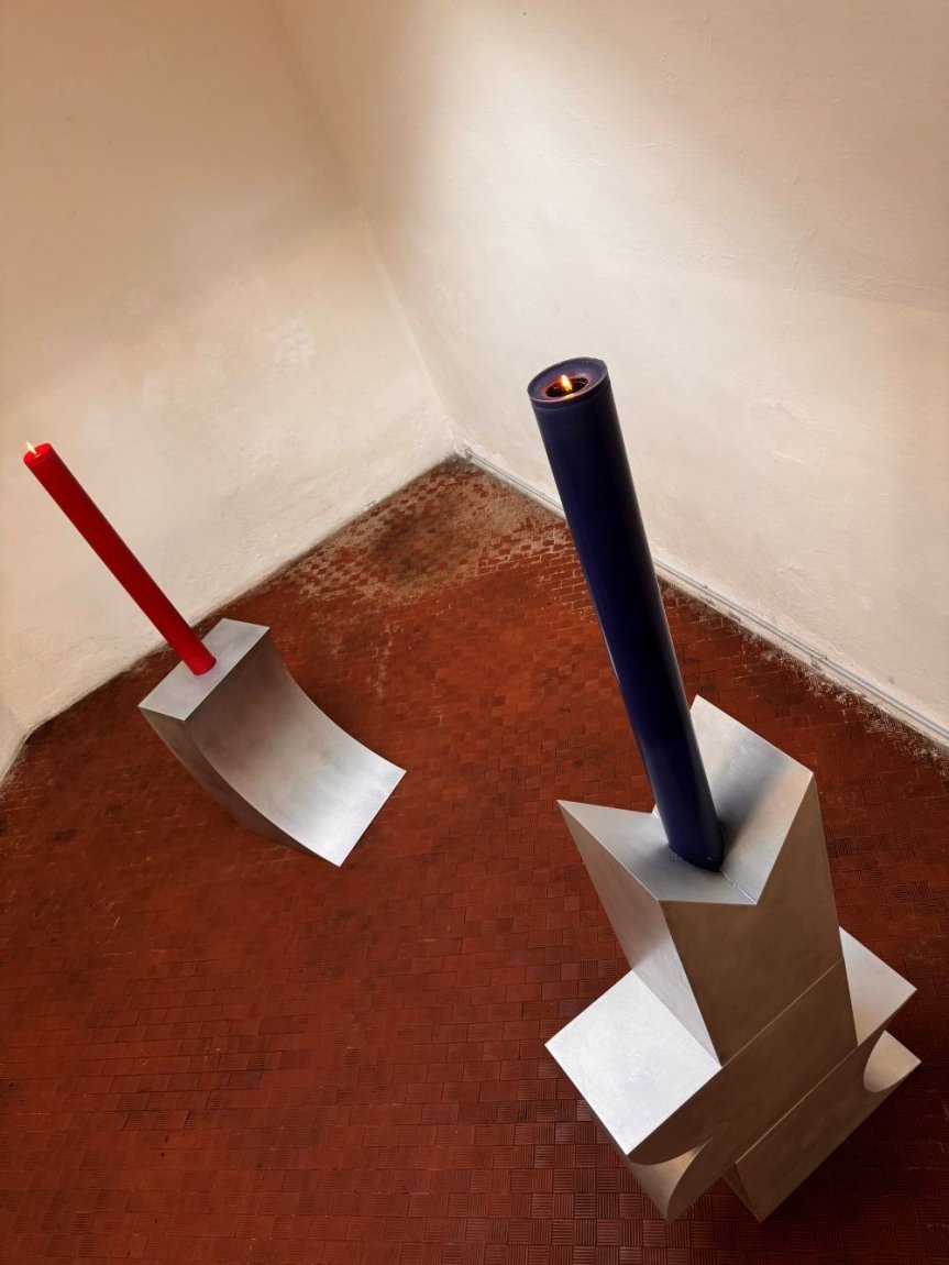 Zwei Metallskulpturen im Eckraum: hohes blaues Rohr mit Flamme, kürzeres rotes Rohr.