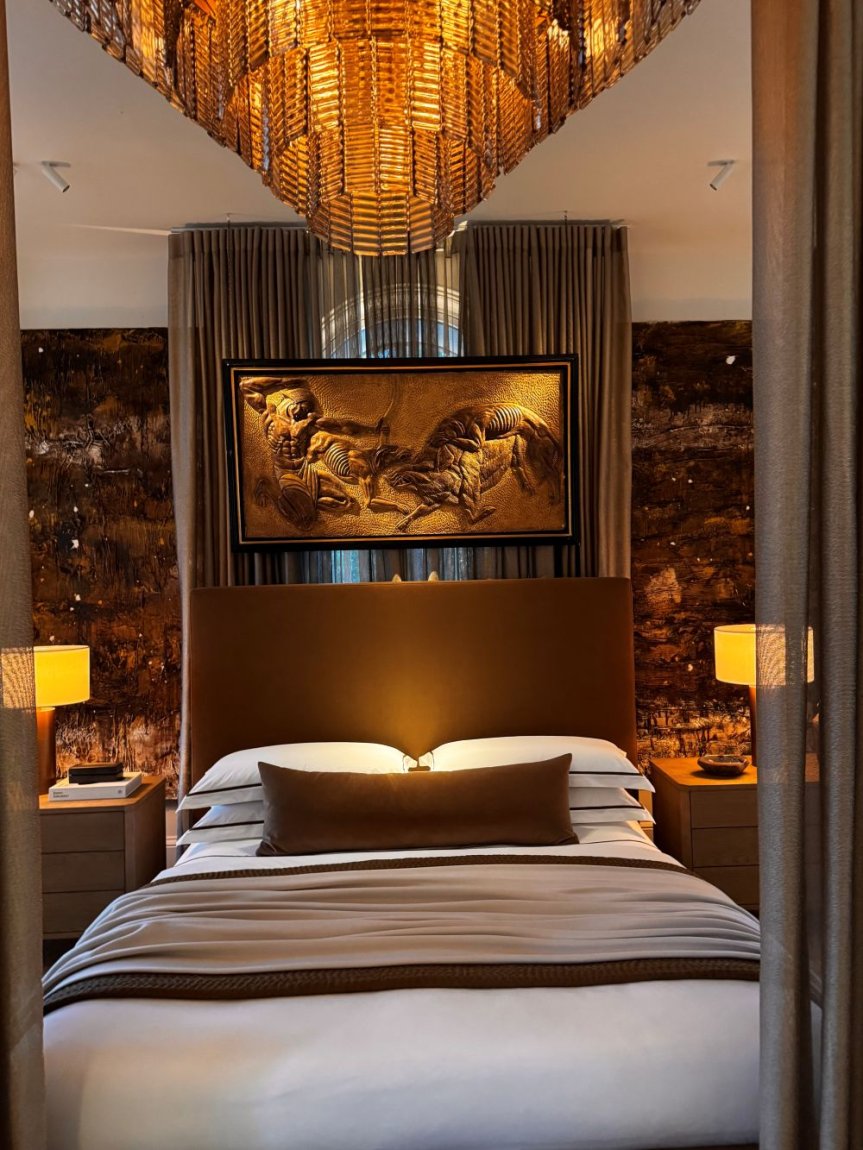 Fotografie: Schlafzimmer mit Polsterbett, Kronleuchter, Nachttischlampen, gerahmtes Bild überm Bett.