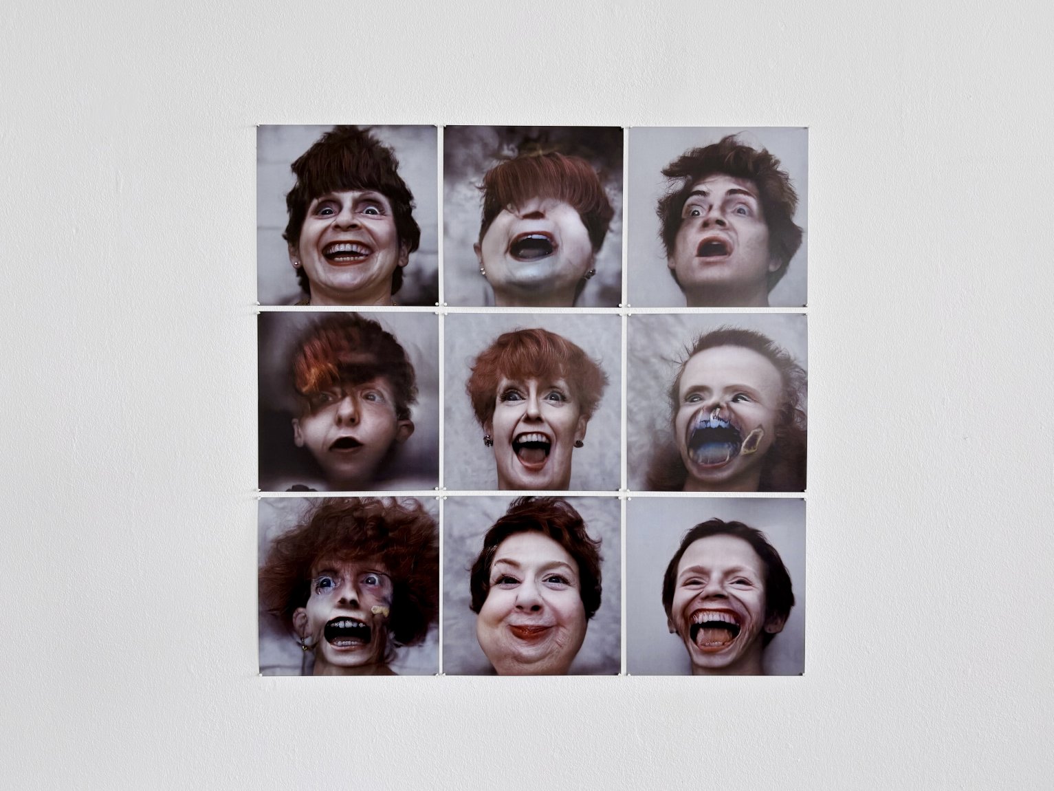 Neun Porträtfotos im 3x3 Raster; Nahaufnahmen offener Münder, an weißer Wand installiert.