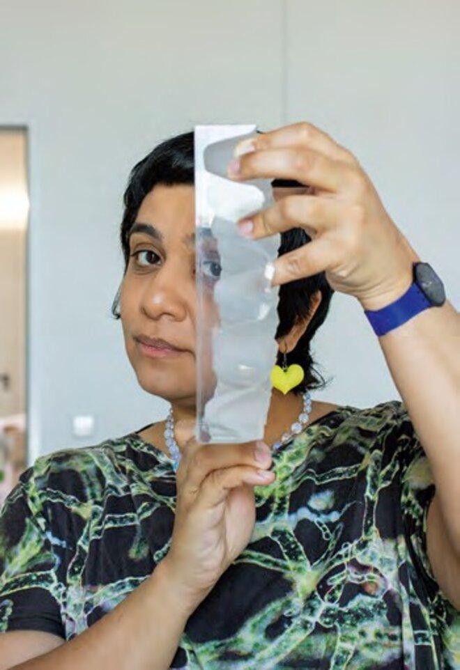 Foto: Die Küntlerin Monira Al Qadiri hält vertikalen transparenten Block mit runden Aussparungen, blickt konzentriert.