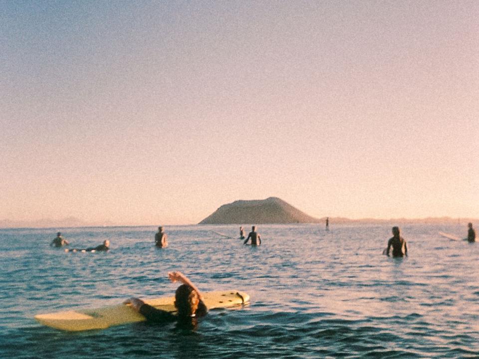 Fotografie: Mehrere Surfer im ruhigen Meer bei Dämmerung, Insel am Horizont.