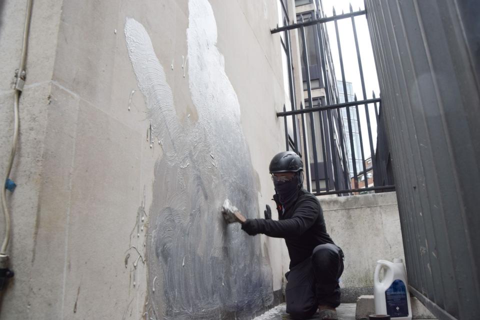 Eine Person schrubbt 2025 ein Banksy-Kunstwerk an den Royal Courts of Justice in London ab, das einen Richter zeigte, der einen Demonstranten mit einem Hammer schlägt