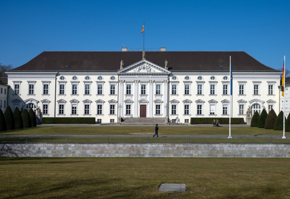 Foto: Schloss Bellevue, Frontansicht der klassizistischen Fassade mit Rasen und Flaggen.