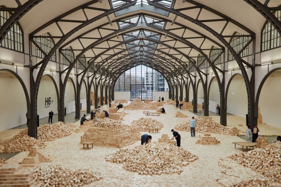 Rauminstallation: große Halle mit bodenfüllenden Haufen heller Holzklötze; Besucher dazwischen.