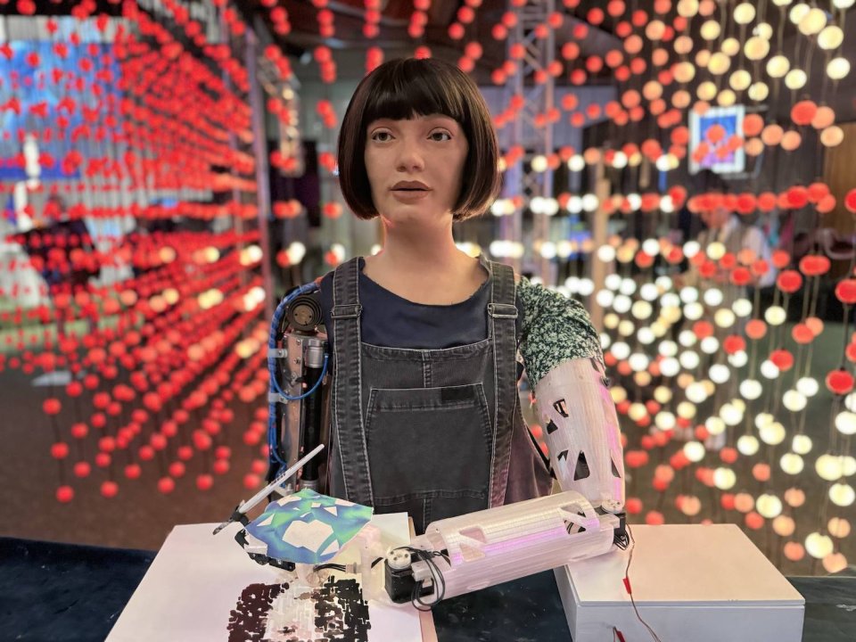 Humanoider Roboter malt am Tisch; Hintergrund aus roten und weißen Lichtpunkten.