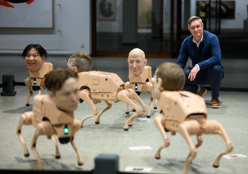 Foto, Installationsansicht: mehrere hundegroße Roboterhunde mit realistischen Köpfen; Besucher