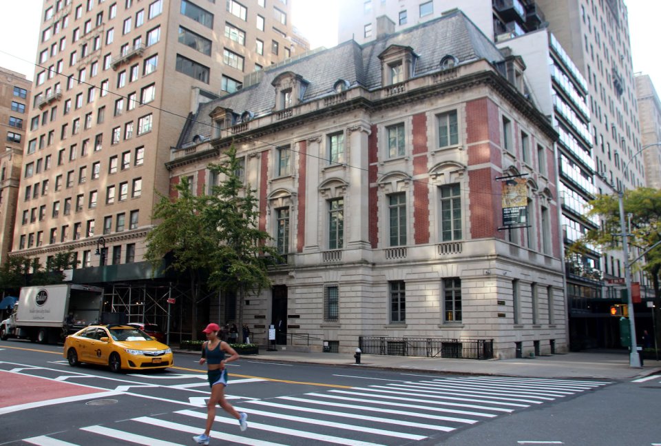 Eckhaus im Beaux-Arts-Stil mit Mansarddach; Jogger am Zebrastreifen, gelbes Taxi an Kreuzung.