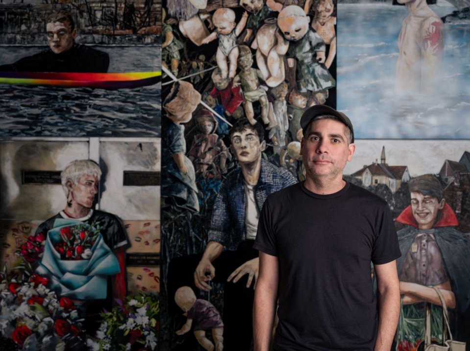 Porträtfoto: Künstler in schwarzem T‑Shirt vor Wand mit großformatigen figurativen Gemälden.