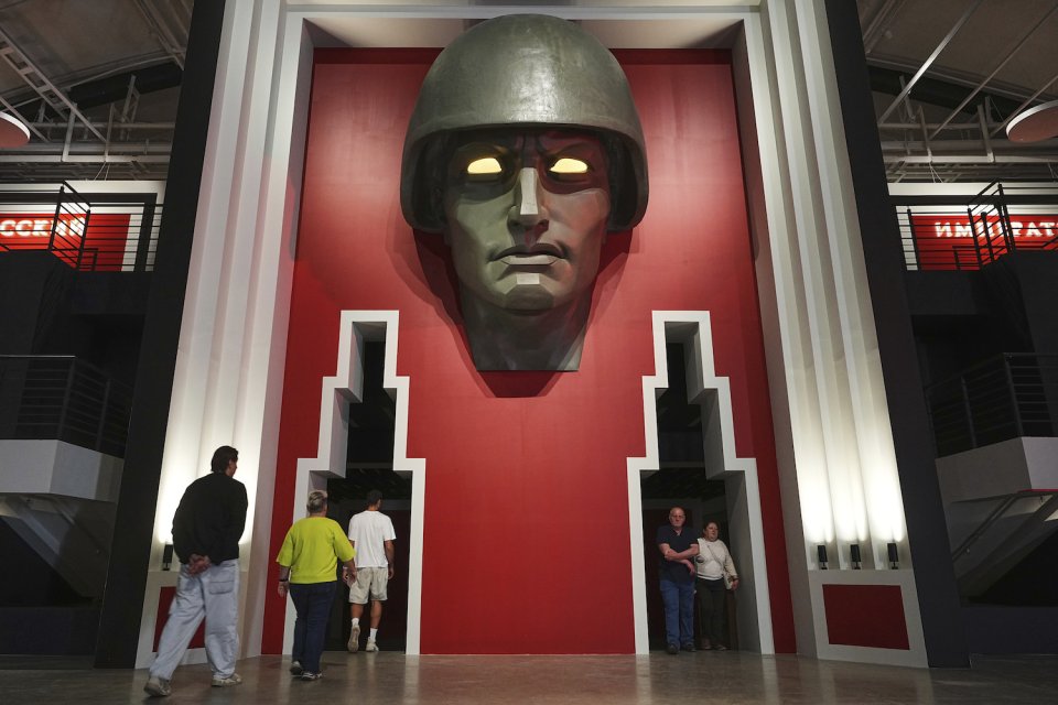 Installationsansicht: monumentale Kopfskulptur mit Helm über zwei Eingängen, leuchtende Augen.