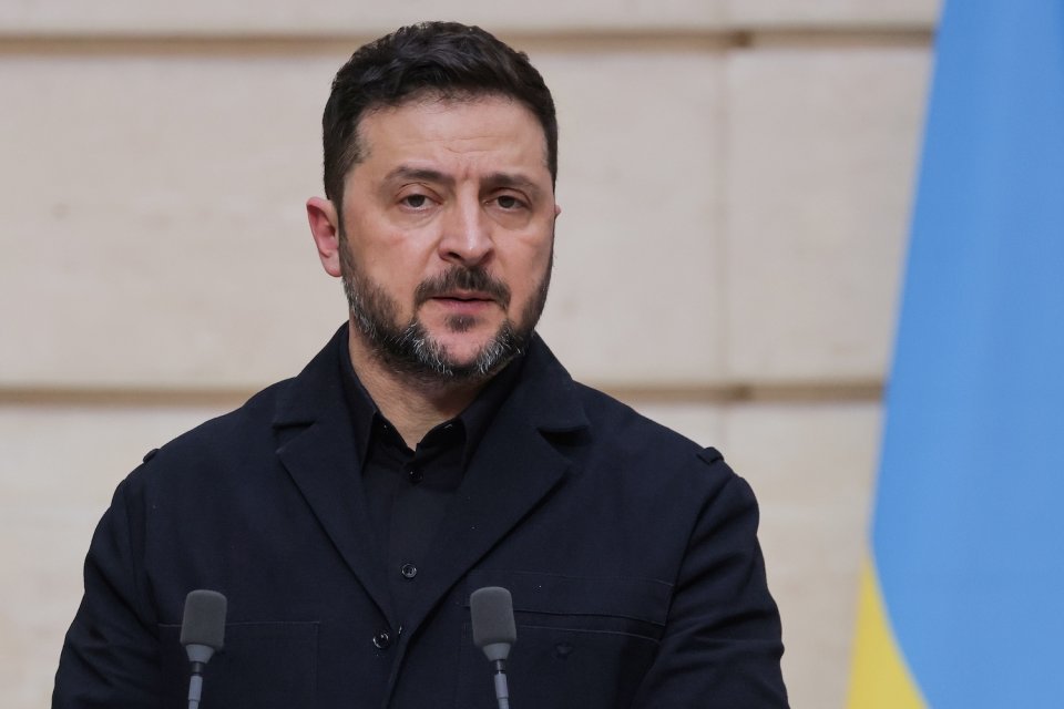 Foto: Redner bei Pressekonferenz, zwei Mikrofone, ukrainische Flagge im Hintergrund.
