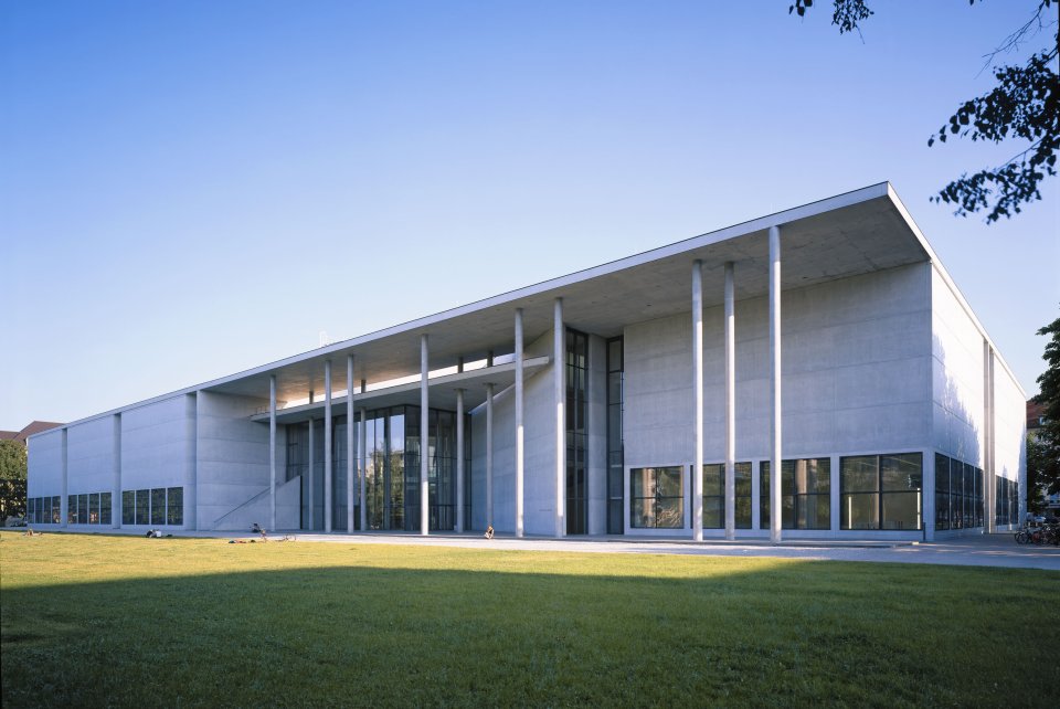 Außenansicht Pinakothek der Moderne, München: kubischer Betonbau mit Säulenreihe, Rasen davor.