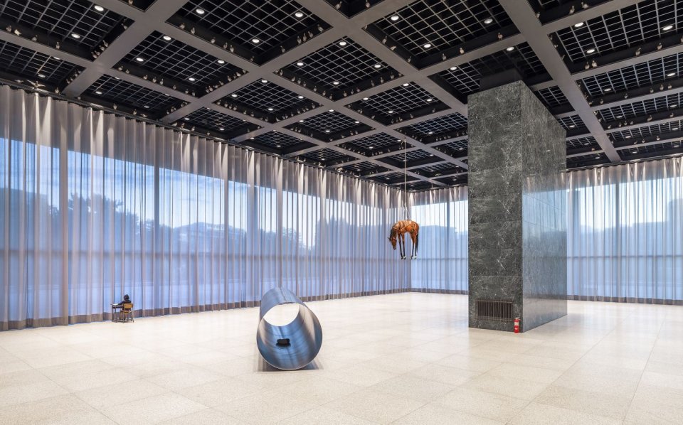 Installationsansicht: weiter verglaster Saal; Metallform am Boden, braune Form hängend, kleines Objekt