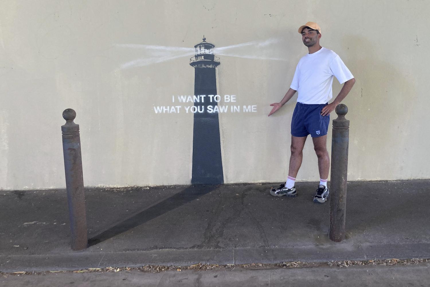 Ein Mann posiert vor einem Kunstwerk von Banksy