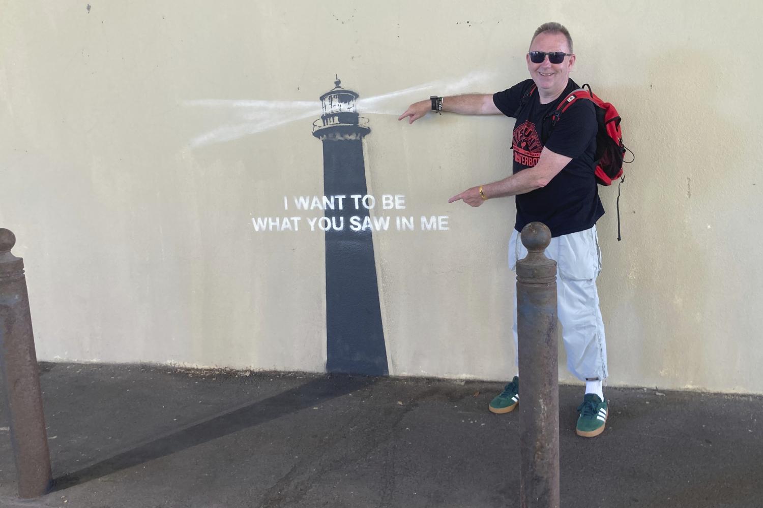 Ein Mann posiert vor einem Kunstwerk von Banksy in Marseille