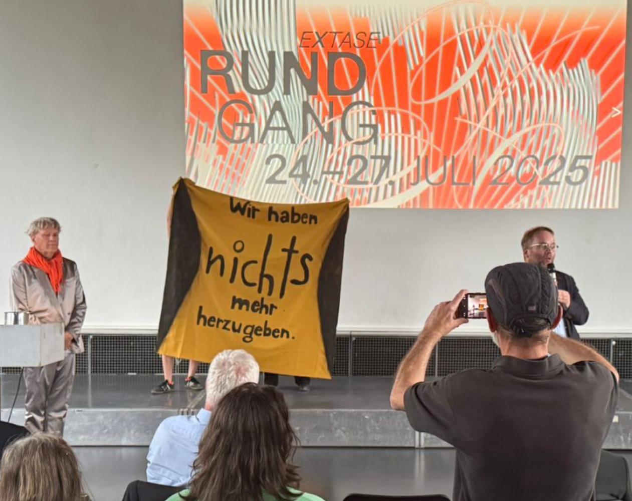 Bjørn Melhus bei seiner Rede zum Rundgang 2025 an der Kunsthochschule Kassel. Rechts im Bild: Der hessische Kultur und Bildungsminister Timon Gremmels (SPD).