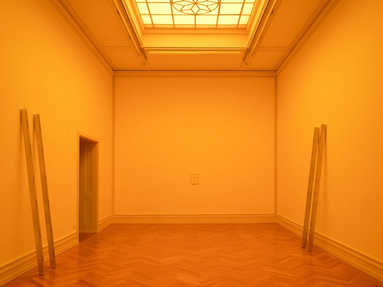 Installationsansicht: monochrom gelber Saal mit Oberlicht; je zwei Latten lehnen an den Wänden.
