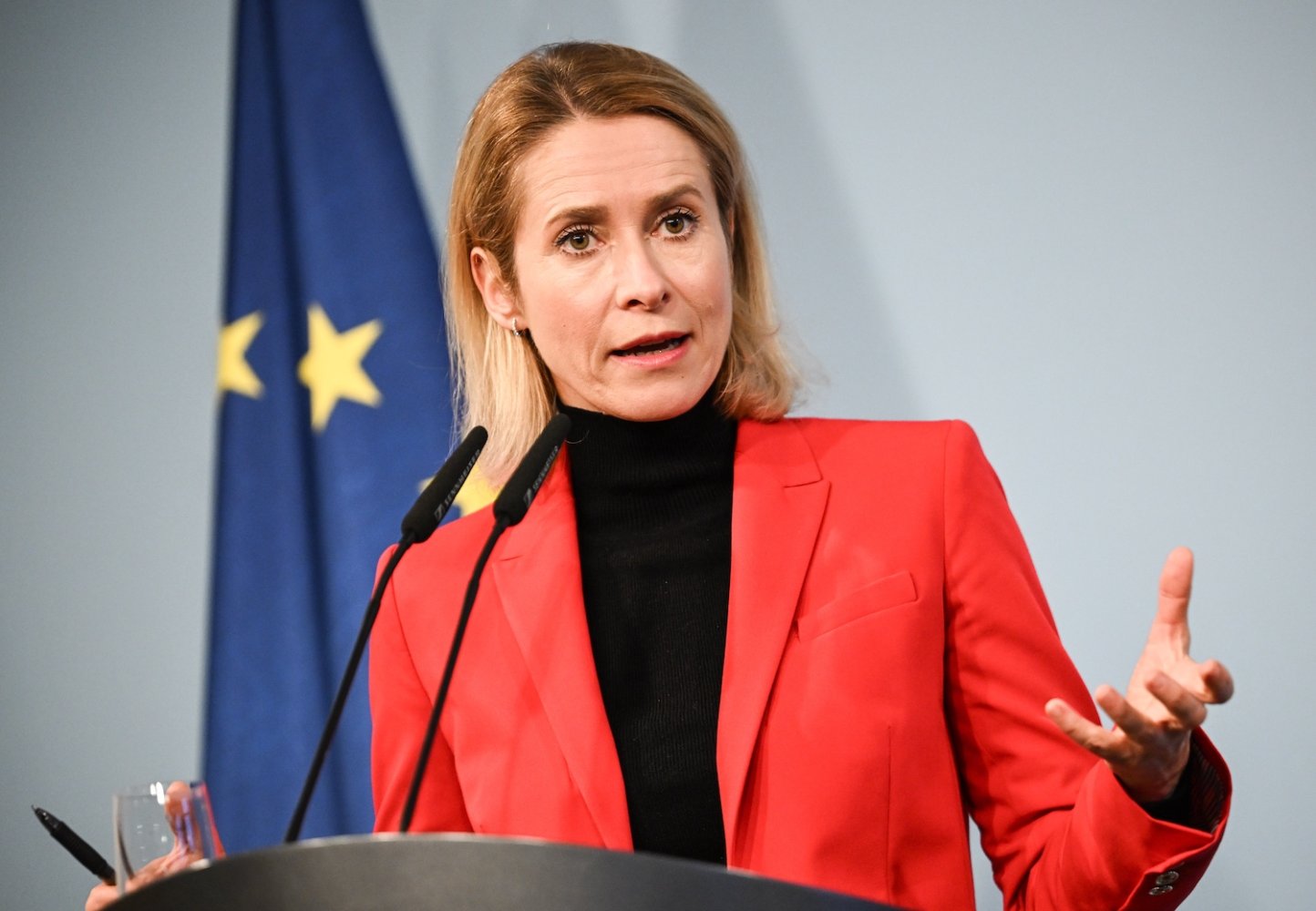Pressekonferenz: Rednerin im roten Blazer am Pult vor EU-Flagge, gestikulierend, Mikrofone.