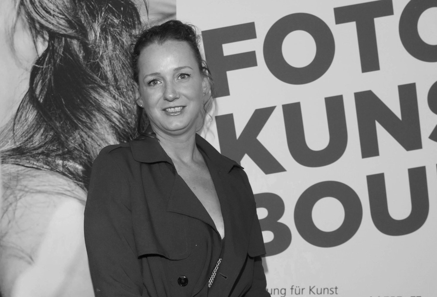 Schwarzweißfoto, Porträt einer Person vor Plakat mit "FOTO KUNS…", leicht lächelnd.
