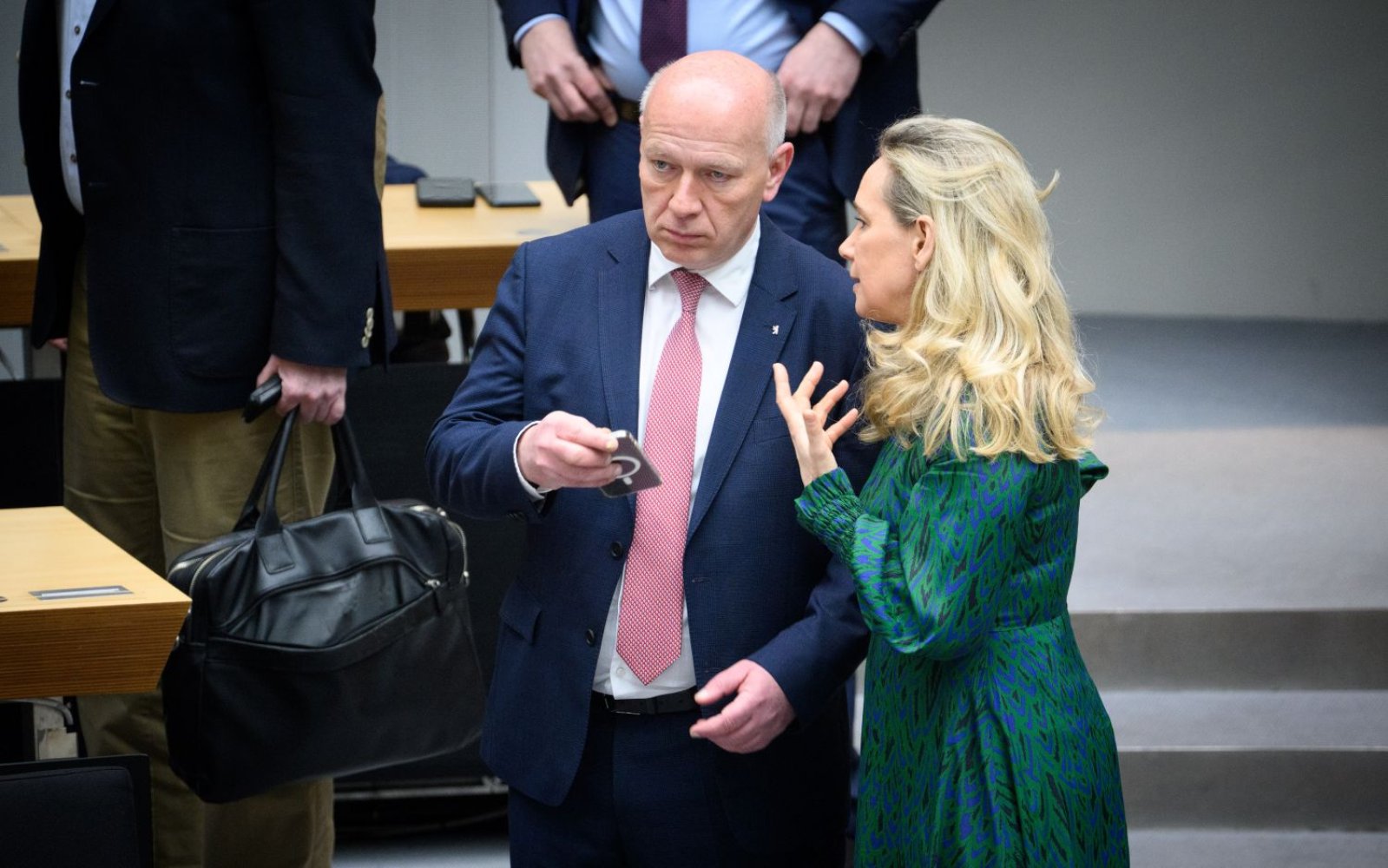 Foto, Sitzungssaal: zwei Personen sprechen; Mann hält Smartphone, Frau gestikuliert.