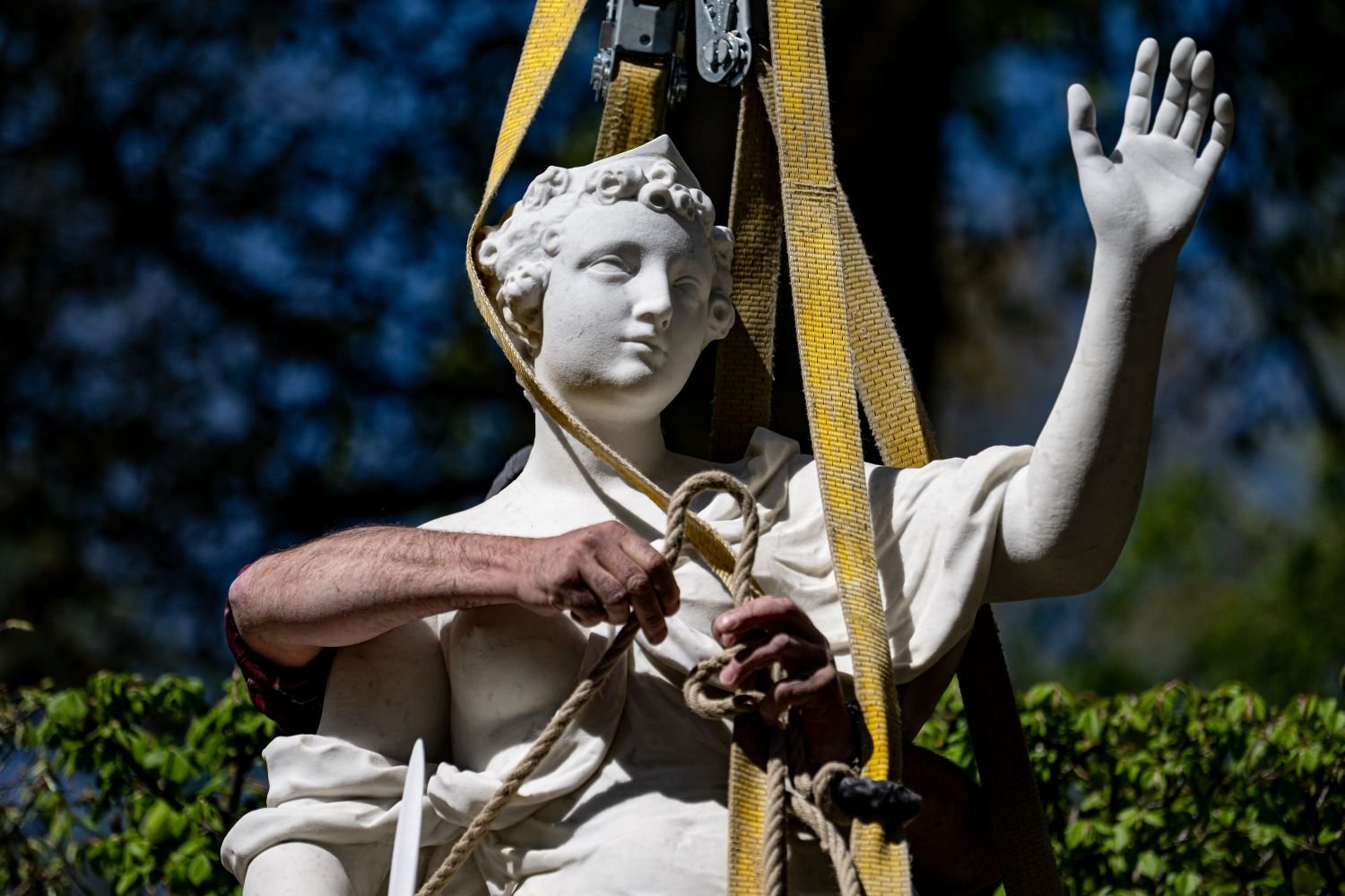 Fotografie: Klassische Marmorskulptur wird mit Hebegurten versetzt; Arbeiterhände sichern Seile.