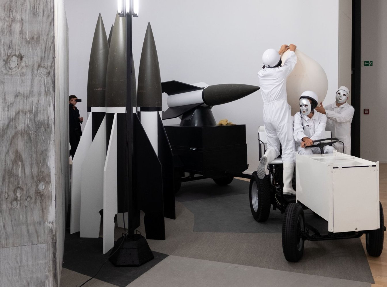 Installationsansicht: Raketenattrappen, Performer in Weiß auf kleinem Wagen, Kunsthalle Gießen
