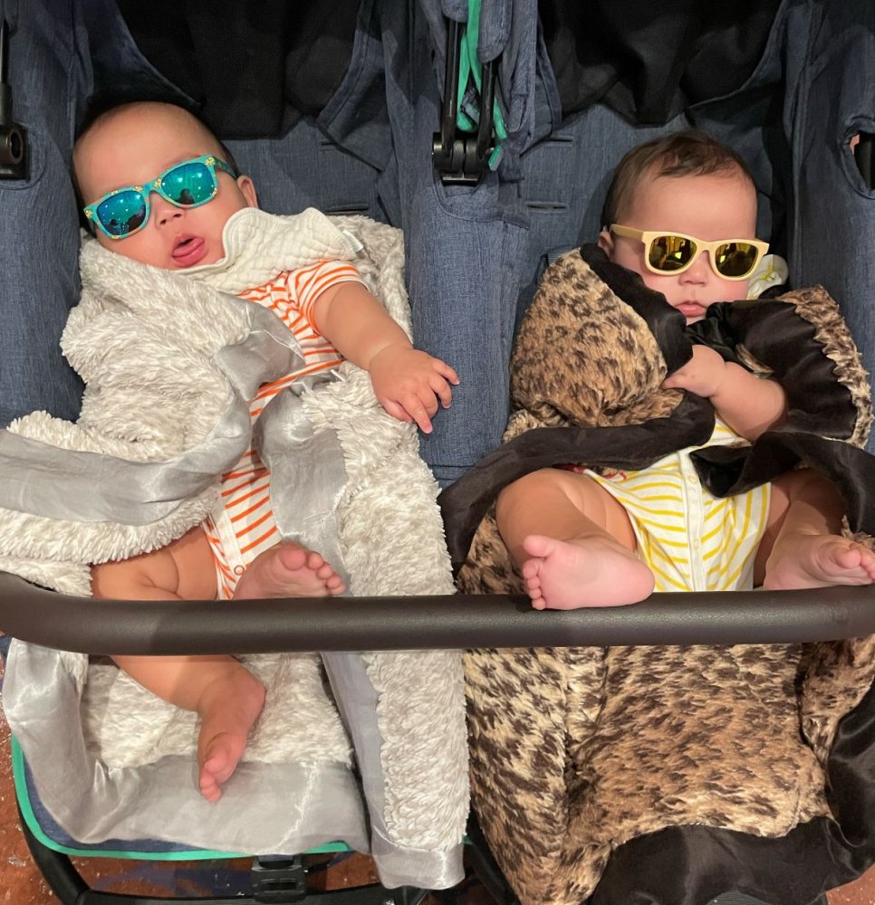 Fotografie: Zwei Babys mit Sonnenbrillen im Doppelkinderwagen, in gemusterten Decken.
