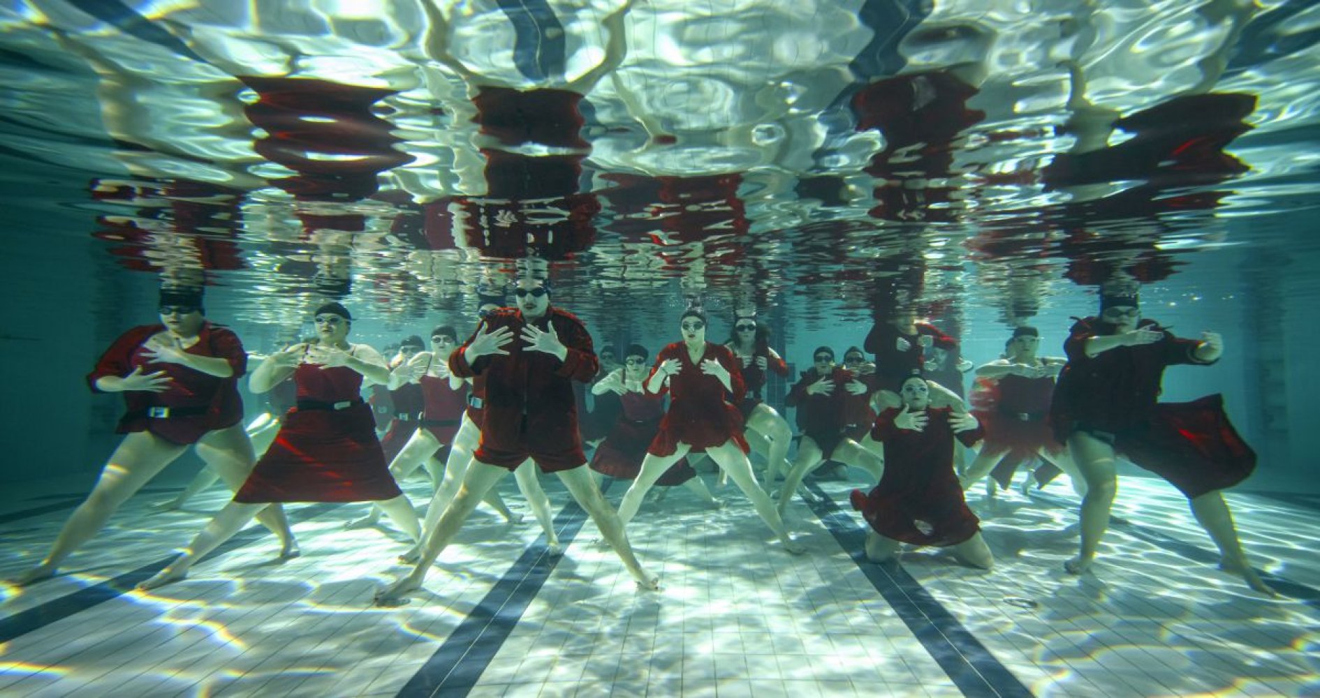 Unterwasser-Foto: große Gruppe in roten Kostümen, breit aufgereiht im Schwimmbecken.