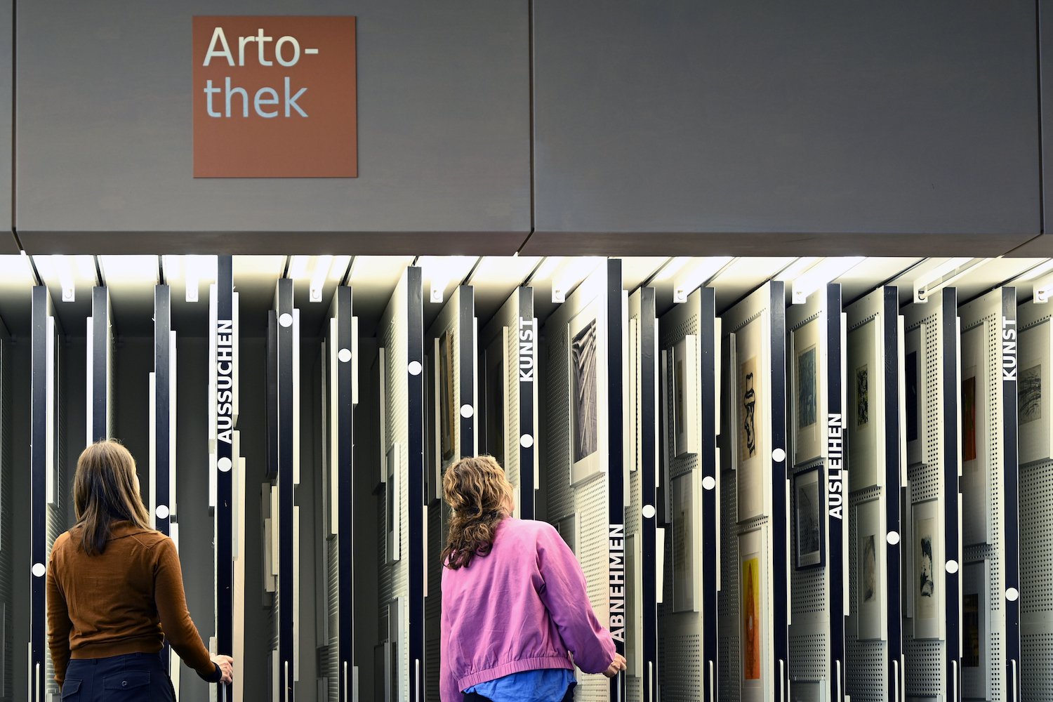 Foto: Artothek, zwei Personen betrachten vertikale Schiebewände mit Kunstwerken.