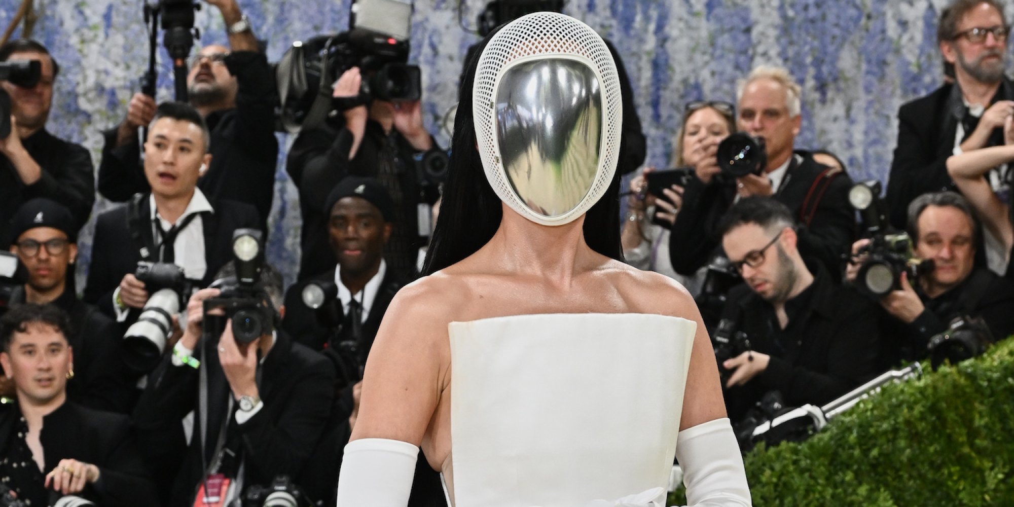 Foto einer Person mit verspiegelter Helmmaske in weißer Robe auf rotem Teppich; Fotografen dahinter.