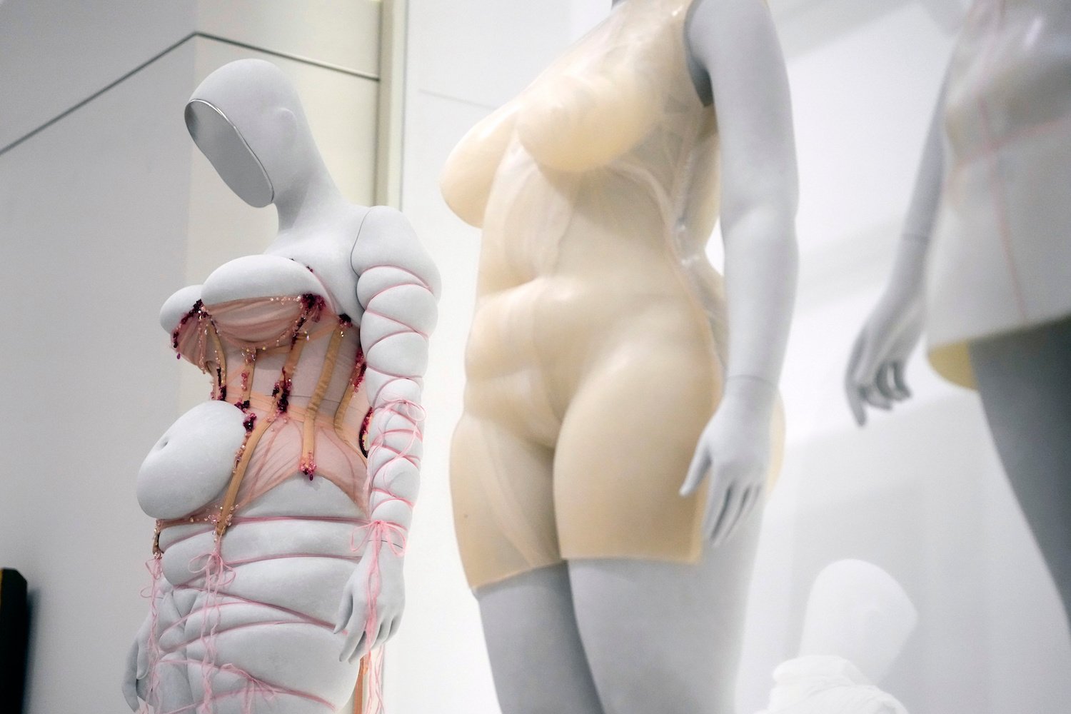 Installationsansicht: Mannequins mit hautfarbenem Body und geschnürtem, gepolstertem Anzug.