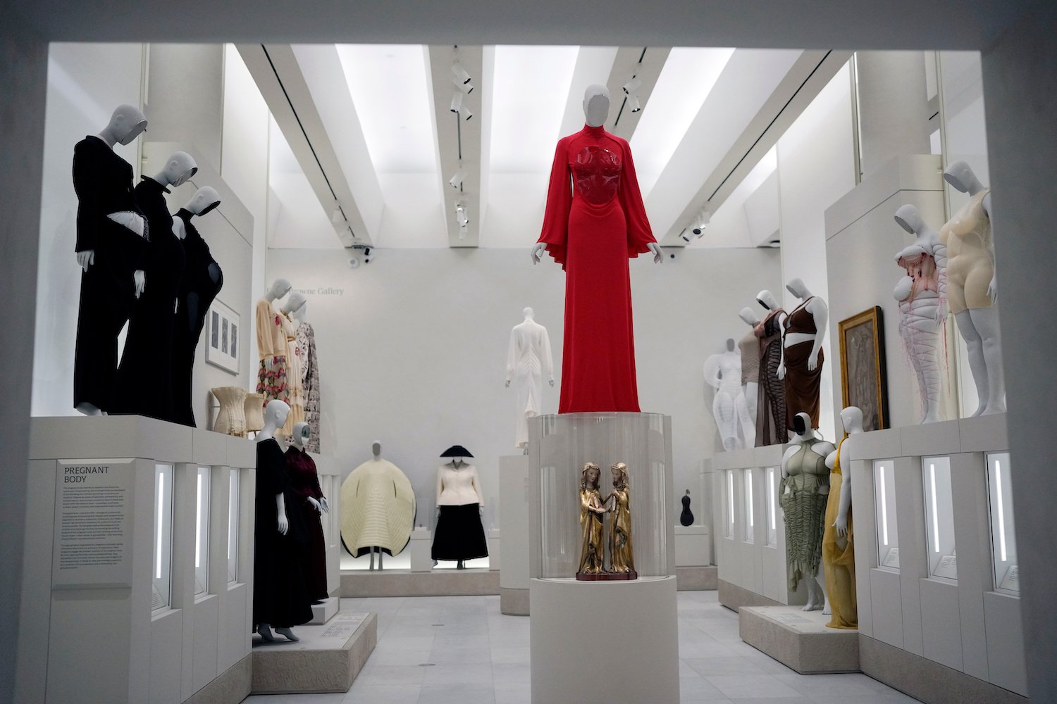 Installationsansicht Modeausstellung: rotes Kleid zentral erhöht, Mannequins auf Sockeln.
