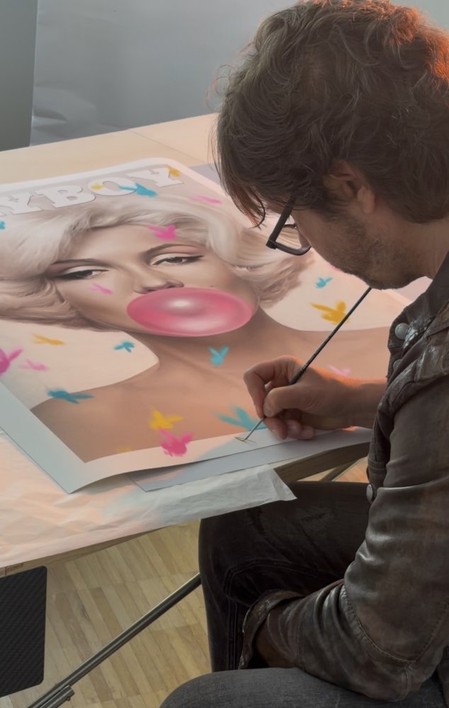 Künstler arbeitet im Studio an Porträt einer Frau mit Kaugummiblase und Schmetterlingen auf Papier