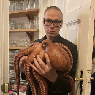 Foto einer Person, die einen großen Oktopus hält; Regal mit Gläsern im Hintergrund